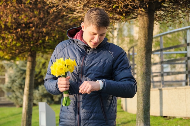 Junger Mann mit Blumenstrauß von Frühlingsblumen betrachtet Armbanduhr