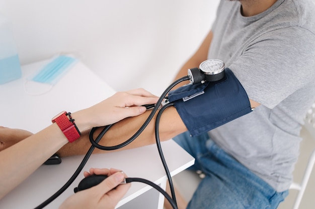 Junger Mann mit Bluthochdruck Ärztin mit Blutdruckmessgerät mit Stethoskopkontrolle