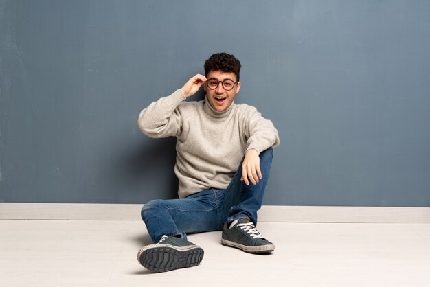 Junger Mann mit Brille auf dem Boden sitzen und überrascht