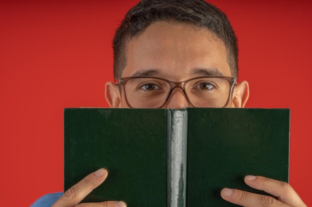 Junger Mann mit Brille, der ein gebundenes Buch vor sein Gesicht hält