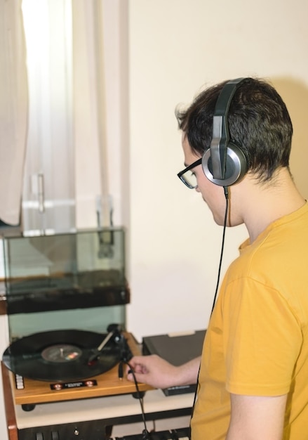 Junger Mann mit Brille genießt es, während er in seinem Zimmer seine Schallplatte mit Vintage-Kopfhörern hört