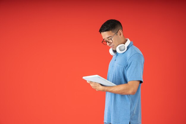 Junger Mann mit Brille liest auf einem digitalen Tablet und trägt Kopfhörer im Nacken