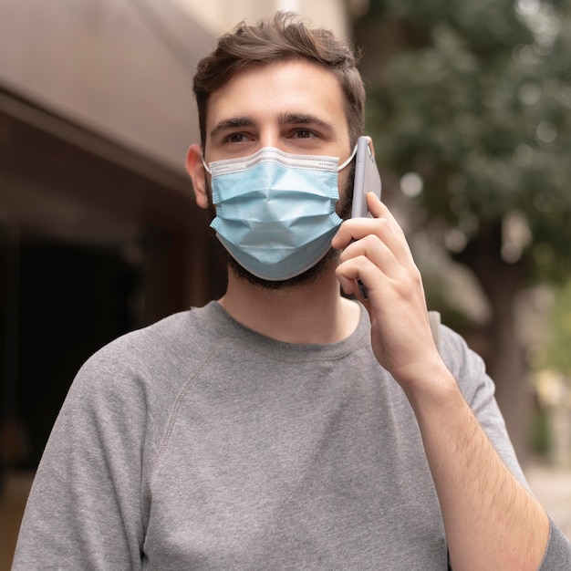 Foto junger mann mit der medizinischen maske, die beim telefonieren geht