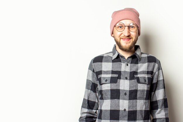 junger Mann mit einem Bart in einem Hut, einem karierten Hemd und einer Brille, die auf einem isolierten Weiß lächeln.