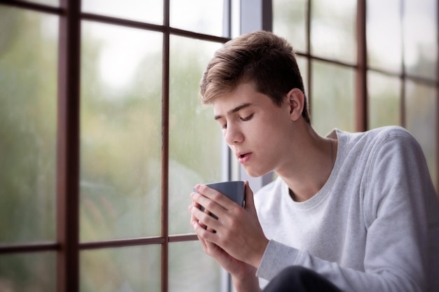 Junger Mann mit einem Becher am Fenster