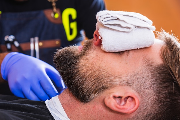 Junger Mann mit einem Handtuch auf den Augen in einem Friseurladen, der darauf wartet, bedient zu werden