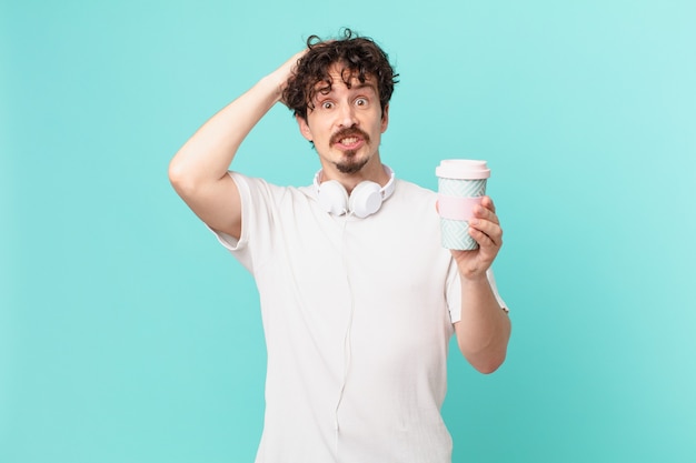 Junger Mann mit einem Kaffee, der sich gestresst, ängstlich oder verängstigt fühlt, mit den Händen auf dem Kopf