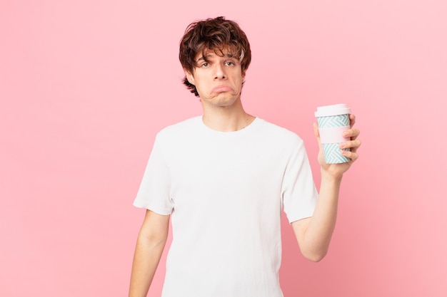 Junger Mann mit einem Kaffee, der traurig und weinerlich ist, mit einem unglücklichen Blick und weint