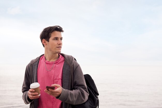 Junger Mann mit einem Kaffee mit einem Handy