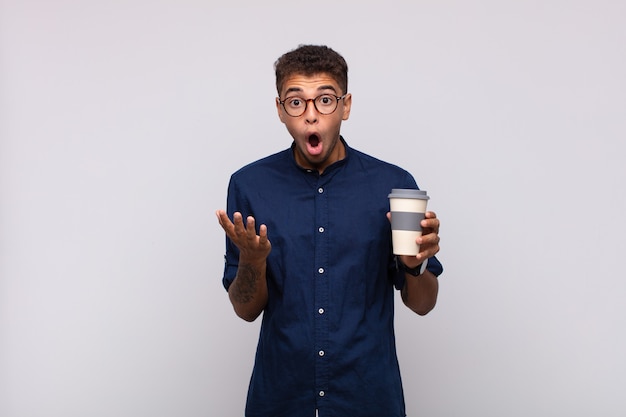Junger Mann mit einem Kaffee mit offenem Mund und erstaunt, schockiert und erstaunt über eine unglaubliche Überraschung