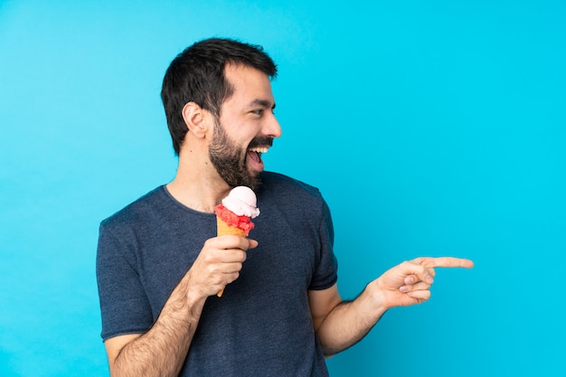 Junger Mann mit einem Kornetteis über blau zeigendem Finger zur Seite und präsentiert ein Produkt