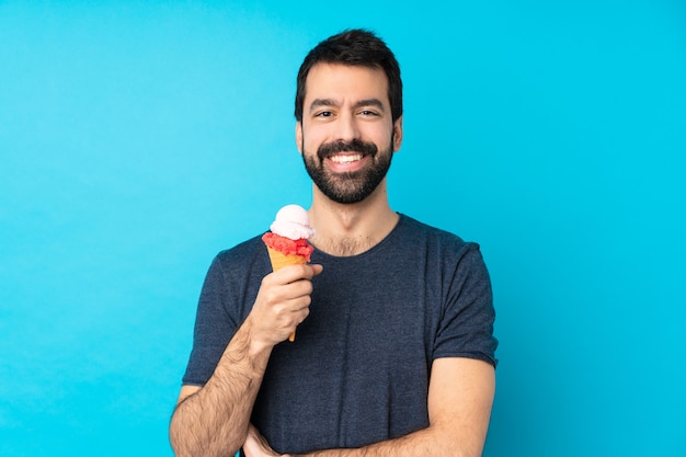 Junger Mann mit einem Kornetteis über isolierter blauer Wand, die die Arme in Frontalposition verschränkt hält