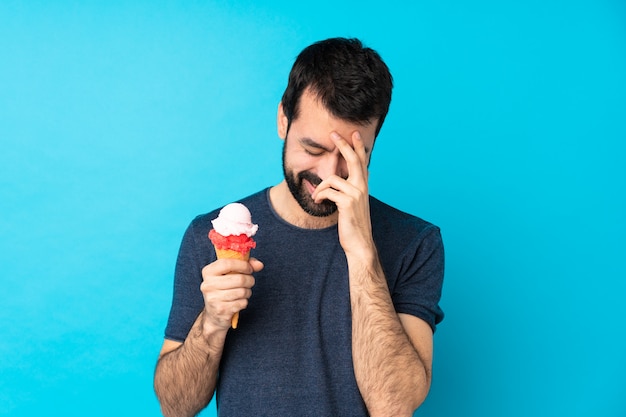 Junger Mann mit einem Kornetteis über isolierter blauer Wand lachend