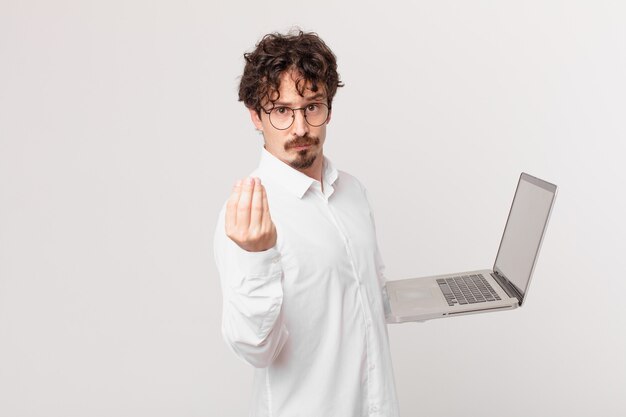 Junger Mann mit einem Laptop, der eine Capice- oder Geldgeste macht und Ihnen sagt, dass Sie bezahlen sollen?