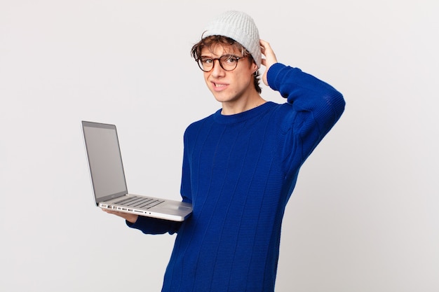 Junger Mann mit einem Laptop, der sich gestresst, ängstlich oder verängstigt fühlt, mit den Händen auf dem Kopf