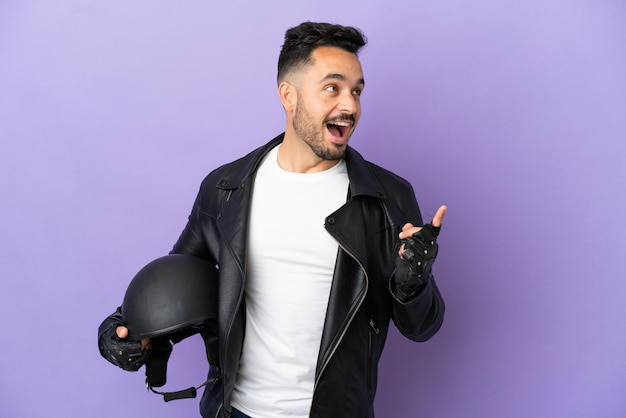 Junger Mann mit einem Motorradhelm, der auf violettem Hintergrund isoliert ist und beabsichtigt, die Lösung zu realisieren, während er einen Finger hochhebt