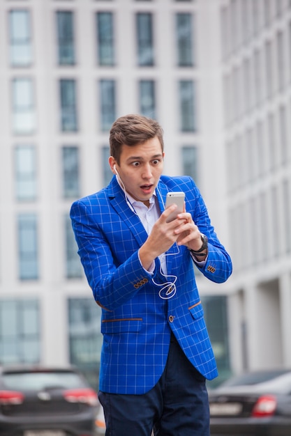 Junger Mann mit einem Telefon und Kopfhörern am Gebäude