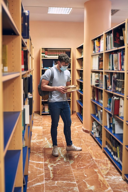 Junger Mann mit einer Maske liest Bücher in der Universitätsbibliothek