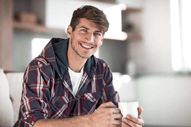 Junger Mann mit einer Tasse Kaffee im Hintergrund in der Küche