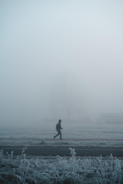Junger Mann mit Gesichtsmaske, der allein auf Bürgersteig im tiefen Nebel geht