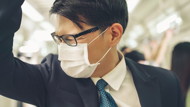 Junger Mann mit Gesichtsmaske fährt in einer überfüllten U-Bahn