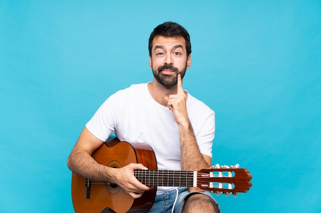 Junger Mann mit Gitarre über getrenntem blauem Hintergrund, der vorder schaut
