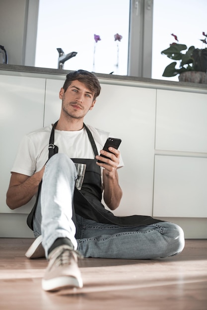 Junger Mann mit Glas Wasser liest SMS auf seinem Handy