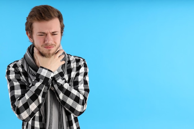 Junger Mann mit Halsschmerzen auf blauem Hintergrund