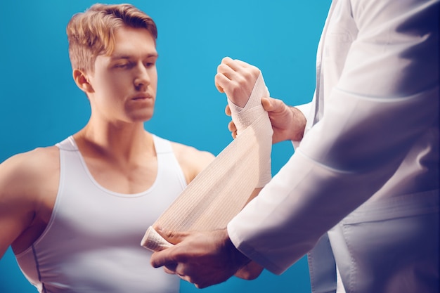 junger Mann mit Handverletzung in der Arztpraxis Der Arzt macht dem Patienten einen Verband