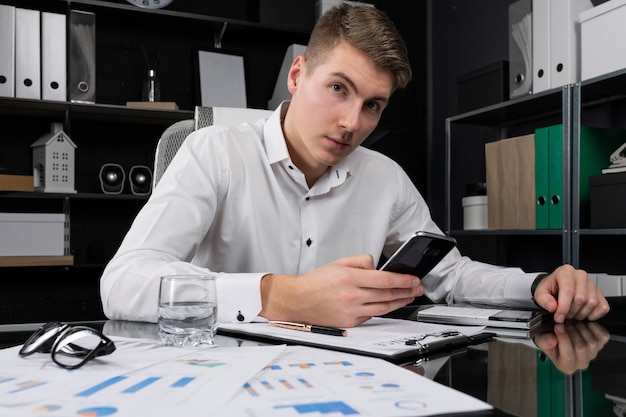 Junger Mann mit Handy in seinen Händen, die bei Tisch im hellen Büro sitzen