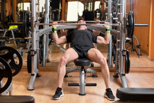 junger Mann mit Hantel Muskeln spielen und Bankdrücken im Fitnessstudio