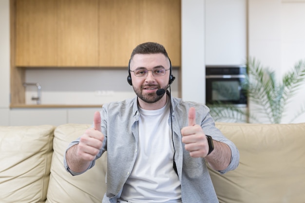 Junger Mann mit Headset, der vorne schaut und Video-Chat im Heimbüro verwendet