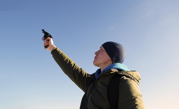 Junger Mann mit Hut schießt mit Waffe in den blauen Himmel