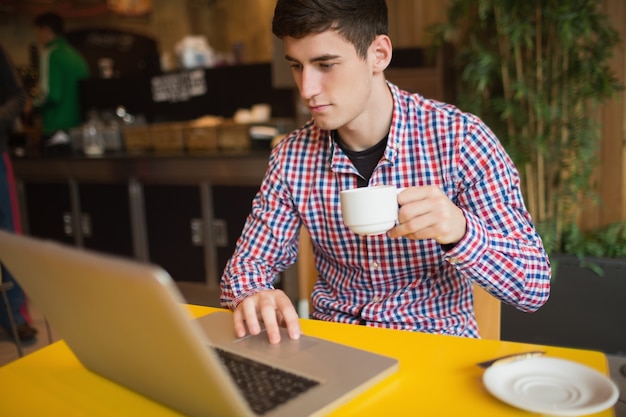 Junger Mann mit Kaffee unter Verwendung des Laptops