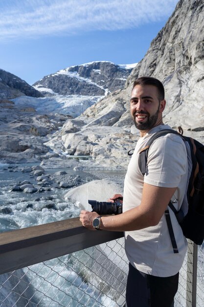 Junger Mann mit Kamera in der Hand, der glücklich den Nigardsbreen-Gletscher in Norwegen besucht