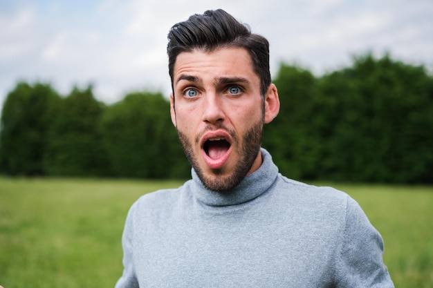 Junger Mann mit klaren Augen mit einem Gesicht großer Überraschung draußen im Park