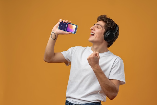 Junger Mann mit Kopfhörern, der Handy benutzt, während er Musik auf gelbem Hintergrund hört