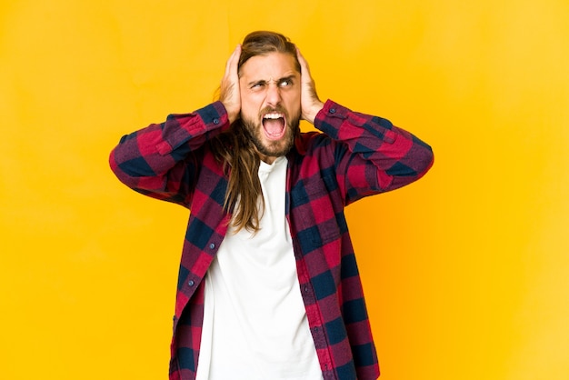 Junger Mann mit langem Haarblick bedeckt Ohren mit Händen, die versuchen, nicht zu lautes Geräusch zu hören.