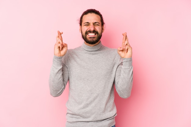 Junger Mann mit langen Haaren auf einer rosa Wand, die Finger kreuzt