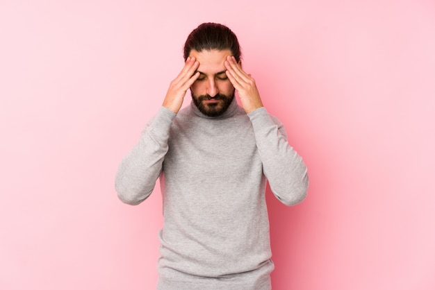 Junger Mann mit langen Haaren auf einer rosa Wand, die Schläfen berührt und Kopfschmerzen hat.