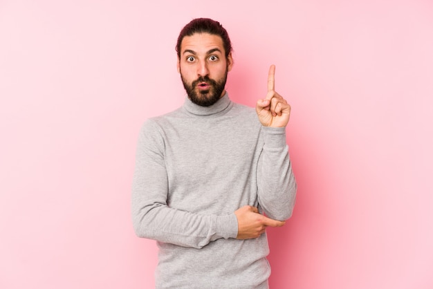 Junger Mann mit langen Haaren, isoliert auf einer rosa Wand, die eine große Idee hat