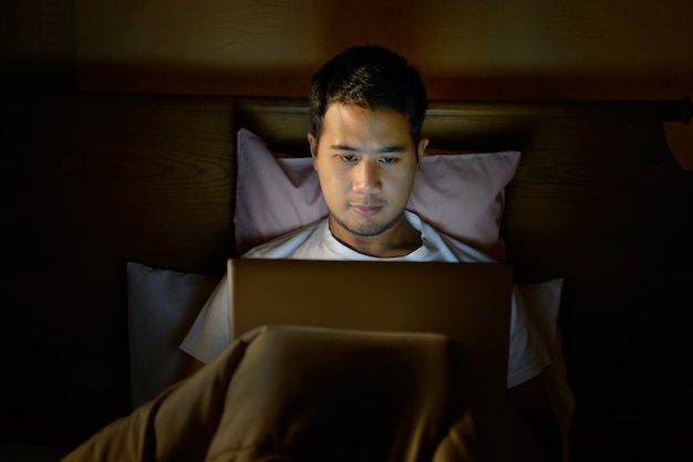 Junger Mann mit Laptop in seinem Bett in der Nacht