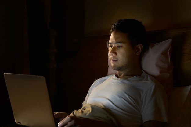 Junger Mann mit Laptop in seinem Bett in der Nacht