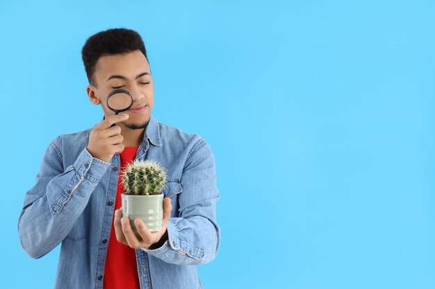 Junger Mann mit Lupe und Kaktus auf blauem Hintergrund