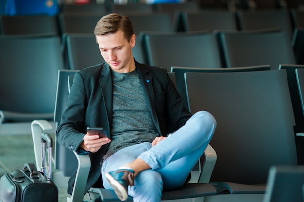 Junger Mann mit Mobiltelefon am Flughafen beim Warten auf Einstieg.