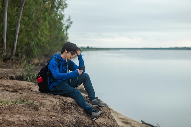 Junger Mann mit Rucksack mit seinem Smartphone am Rande eines Berges, aktiver Lebensstil.