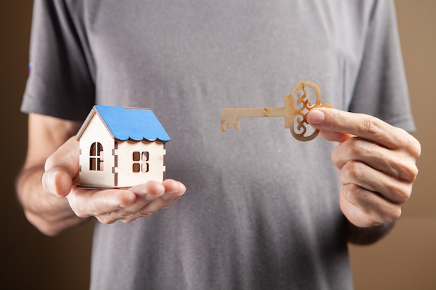 Junger Mann mit Schlüsseln und Scheinhaus auf braunem Hintergrund