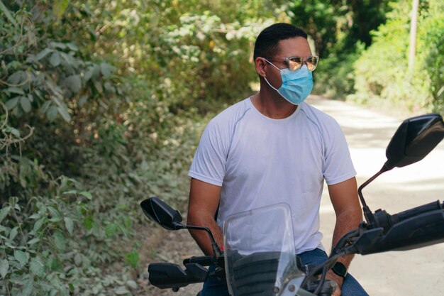 Junger Mann mit Schutzmaske und Sonnenbrille auf einem Motorrad auf einer Landstraße