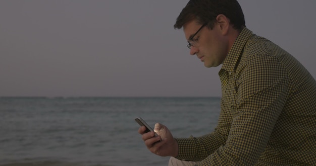 Junger Mann mit Smartphone auf dem Seeweg am Abend using