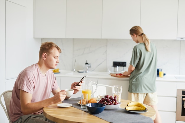 Junger Mann mit Smartphone, das Kaffee durch gediente Tabelle hat